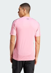 Lyserød atletisk t-shirt med korte ærmer, meshstruktur på skuldrene og sorte detaljer. Har 'Freedom & Dream' logoet på ryggen.