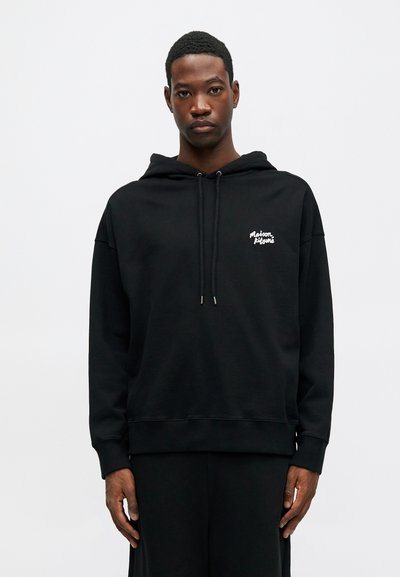 Hanorac negru cu glugă, realizat dintr-un material moale, având manșete riboljite și un mic logo alb pe partea stângă a pieptului. Design simplu.