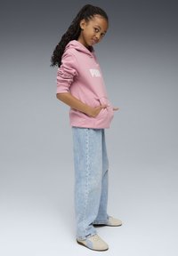 Rosa Kapuzenpullover mit Fronttasche und weißem Logo, kombiniert mit hellblauen weiten Jeans und beigen Sneakern mit hellblauen Akzenten.