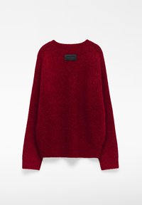 Czerwony, oversize sweter wykonany z miękkiego, teksturowanego materiału. Posiada okrągły dekolt oraz prostokątną czarną metkę z tyłu.