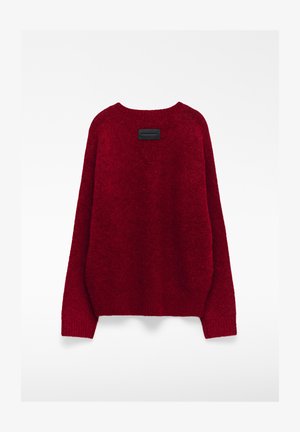 Rode, oversized trui gemaakt van zachte, gestructureerde stof. Heeft een ronde halslijn en een rechthoekig zwart label op de achterkant.