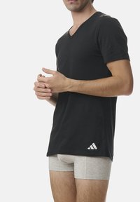 Black v-neck t-shirt made of cotton with short sleeves, featuring a white Adidas logo on the lower left side. Worn with light gray boxer shorts.