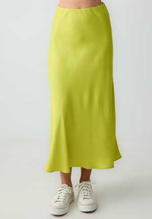 Gonna maxi in tessuto verde lime, liscia, con vita aderente e orlo fluente, abbinata a sneakers bianche con suola platform.