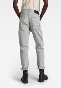Pantalones de mezclilla gris con un corte relajado, que cuentan con bolsillos traseros y puños enrollados, combinados con botas negras hasta el tobillo, mostrando un atuendo casual.