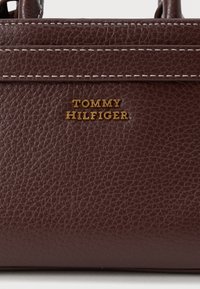 Borsa a tracolla in pelle marrone con texture, caratterizzata dal logo "TOMMY HILFIGER" in tonalità dorata, dettagli a cucitura superiore e una forma strutturata.