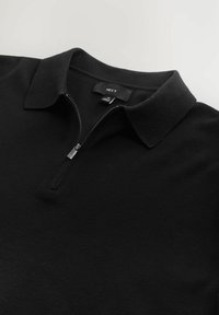 Sort pullover med lynlås ved halsen, flad krave og blødt tekstureret stof. Etiketten er synlig med mærkenavnet 'NEXT'.