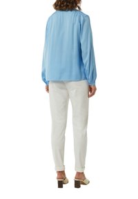 Jasnoniebieska bluzka z długim rękawem i marszczonym tyłem, zestawiona z białymi wąskimi spodniami. Stylizacja charakteryzuje się prostym wzornictwem i lekkim materiałem.