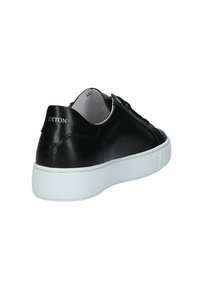 Sneaker in pelle nera con suola in gomma bianca, caratterizzata da dettagli cuciti e una texture liscia. Marchio visibile sul tallone.
