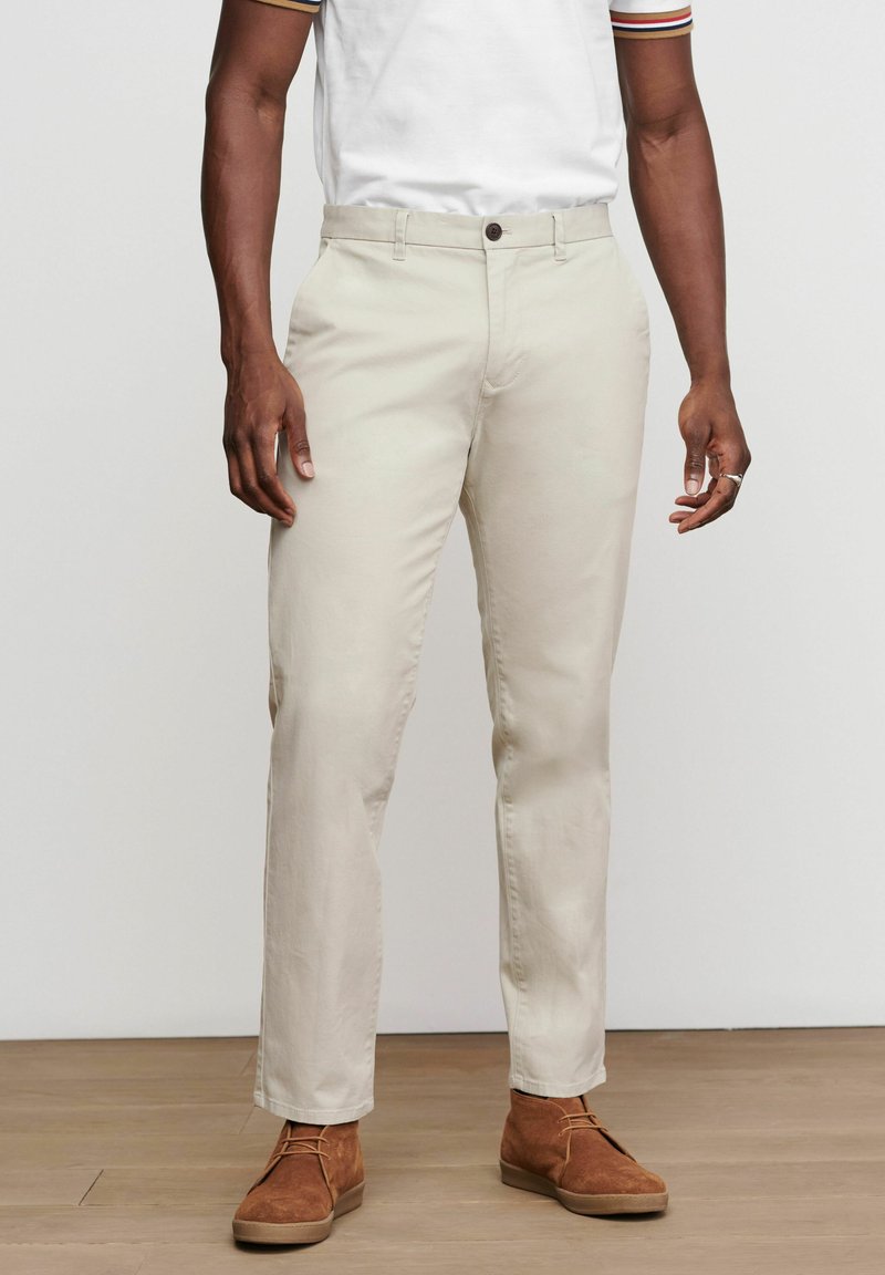 Beige bomulds chinos med lige pasform, en enkelt knaplukning og sidelommer, parret med brune ruskinds sko.