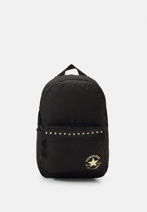 Mochila negra Converse con bolsillo delantero con cremallera, tachuelas doradas sobre el bolsillo y logo dorado de Converse All Star en la parte inferior derecha.