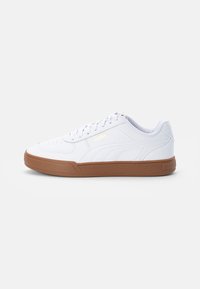 Zapatilla Puma blanca con suela de goma marrón, diseño de cordones y detalle de logo lateral sobre fondo claro.