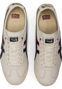 Cream leather sneakers with navy and burgundy accents, featuring a textured insole, flat laces, and a classic design.