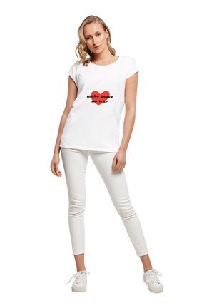 Hvid T-shirt med opkrøllede ærmer, der har et rødt hjertegrafik og teksten "make peace no war" i sort. Sammen med hvide bukser og sneakers.