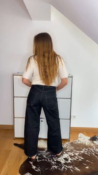 Temno modri široki jeans iz denima z zadnjimi žepi, prikazani poleg svetle pletene majice. Ozadje sestavljajo enobarvne stene in lesena tla.