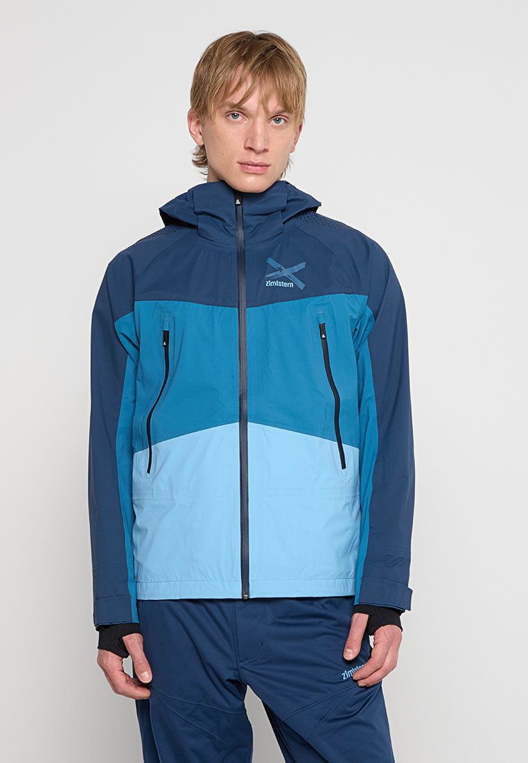 Kurtka w blokach kolorystycznych w odcieniach granatu i turkusu, z zamkiem błyskawicznym z przodu, regulowanym kapturem oraz dwoma zapinanymi na zamek kieszeniami na piersiach. Wykonana z teksturowanego materiału.