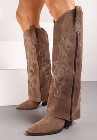 Bottines en daim marron à hauteur de genou avec un bout pointu, des coutures décoratives et une fermeture éclair sur le côté. Présente un design de tige évasée pour un look distinctif.