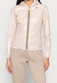 Lyserød hættetrøje lavet af glinsende materiale, med en frontlynlås og multicolor striber, elastiske manchetter og en kropsnær pasform.