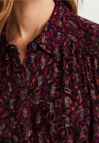 Mörk blommig knapp-up skjorta med en blandning av röda, vinröda och gyllene toner. Strukturerad tyg med metalliska accenter och samlade detaljer.