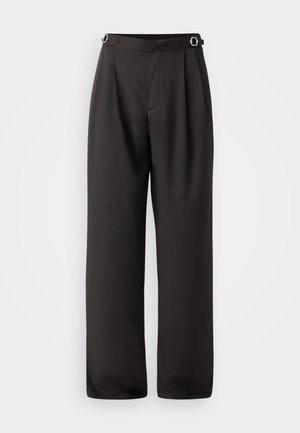 Un pantalon large noir en tissu lisse, avec une taille haute, deux boucles en métal argenté au niveau de la taille, et un design plissé à l'avant.