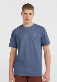 Drengetrøje i blå bomuld med korte ærmer, der har et cirkulært logo på brystet i beige og en afslappet pasform. Glat tekstur.