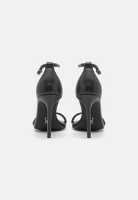 Sandales à talons hauts en cuir noir avec des brides de cheville ajustables, arrière ouvert et talons aiguilles fins. Présente une finition lisse et un design minimaliste.