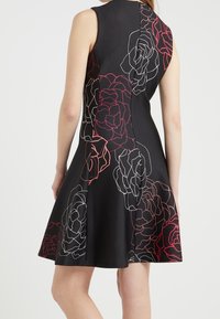 Svart ärmlös klänning med en utsvängd kjol, prydd med vita och röda rosoutlinjer, i ett mjukt tyg med en dragkedja bak.