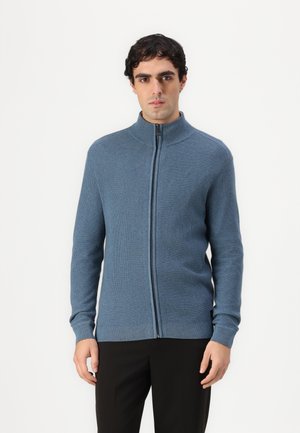 Sudadera azul con cremallera hecha de material acanalado, con un cuello alto y mangas largas, que presenta una textura suave y una silueta ajustada.