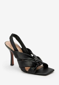 Černé kožené lodičky se zavřenou patou, které se vyznačují uzlovým designem, otevřenou špičkou a čtveratým tvarem špičky. Podpatky mají tenký tvar stiletto.