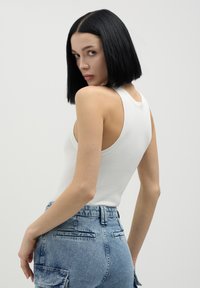 Débardeur blanc côtelé avec un dos nageur, associé à un jean taille haute bleu clair avec une finition texturée et des poches arrière.