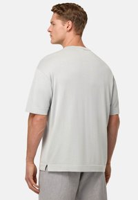 T-shirt grigio a maniche corte con scollatura tonda, vestibilità comoda, spacchi laterali e superficie liscia, indossato con pantaloni chiari a motivo grigio.