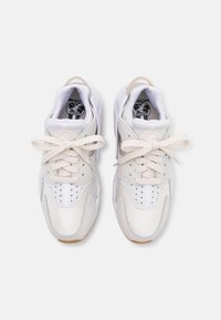 White athletic sneakers with a textured design, featuring light grey accents, a padded collar, and flat laces. Rubber sole with perforations.