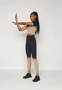 Completo sportivo a due pezzi composto da un top corto beige aderente e leggings neri a vita alta con effetto ombré, texture liscia e cuciture decorative laterali.