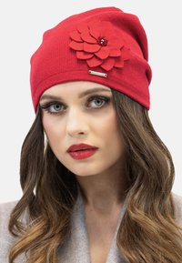 Czerwona dziana czapka beanie z dużym filcowym akcentem w postaci kwiatu, ozdobiona koralikami, z subtelną metaliczną metką na tuszy.
