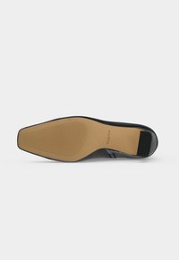 Semelle d’une chaussure de ville noire avec une base beige comportant de fines rainures et le nom de la marque Aldo sur la voûte plantaire.