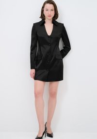 Schwarzes, maßgeschneidertes Minikleid mit tiefem V-Ausschnitt, langen Ärmeln, sechs Knopfverschluss und seitlichen Taschen. Glatte, satinähnliche Textur.