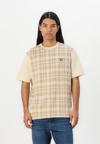 Kortermet t-skjorte i beige med rutete mønster og oransje og brune detaljer. Inkluderer en liten gul logo på brystet.