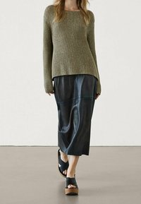 Pull en maille côtelée vert olive à col large, jupe midi en cuir noir, et sandales noires épaisses avec semelles en bois.