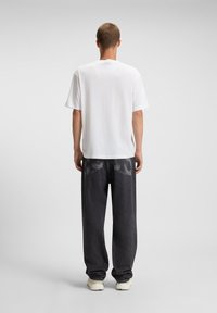 Hvid bomulds T-shirt med afslappet pasform, parret med mørkegrå, løstsiddende jeans med et subtilt falmet mønster.