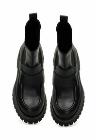 Botas de tobillo de cuero negro con punta redondeada, suela de goma gruesa y un detalle de correa en la parte superior. Textura suave y diseño minimalista.