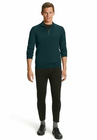 Maglione verde azzurro con collo a zip e maniche lunghe, abbinato a pantaloni neri attillati e sneakers nere. Il tessuto appare liscio e strutturato.