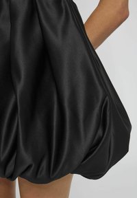 Robe mini en satin noir avec une silhouette volumineuse, présentant un tissu plissé et une texture lisse, créant un drapé ludique à l'ourlet.