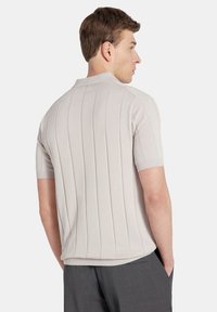 Jasnoszara polo z krótkim rękawem o pionowym prążkowanym wzorze, z kołnierzykiem i dopasowanym krojem, widoczna z tyłu.