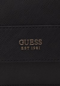 Sort tekstureret pung med "GUESS" logoet og "EST 1981" præget i guld. Glatte syninger langs kanterne og et elegant design.