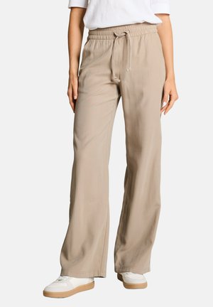 Beige Hose mit weitem Bein, elastischem Bund und Kordelzug, getragen mit weißen Sneakers und einem weißen Hemd.