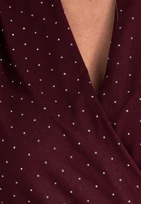 Bordowy materiał z głębokim dekoltem w kształcie V, ozdobiony rozsianymi srebrnymi cyrkoniami, tworzącymi teksturową, błyszczącą powierzchnię.