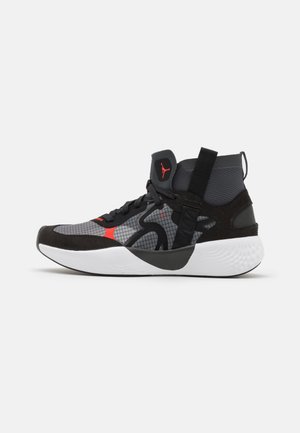 Chaussure de basketball montante noire et grise avec des accents rouges, semelle blanche, matériaux en mesh et en daim, et une languette de traction au talon et à la cheville.