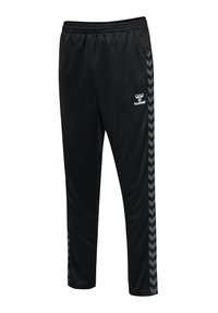 Pantalon de sport noir avec ceinture élastique, bandes chevron grises sur les côtés et logo blanc hummel sur la cuisse droite.
