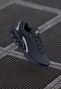 Melnas sporta kurpes ar strukturētu sietu virsmu, izteiktu šņores sistēmu un burbuļveida zoli. Iezīmējas ar baltu akcentu pie papēža.