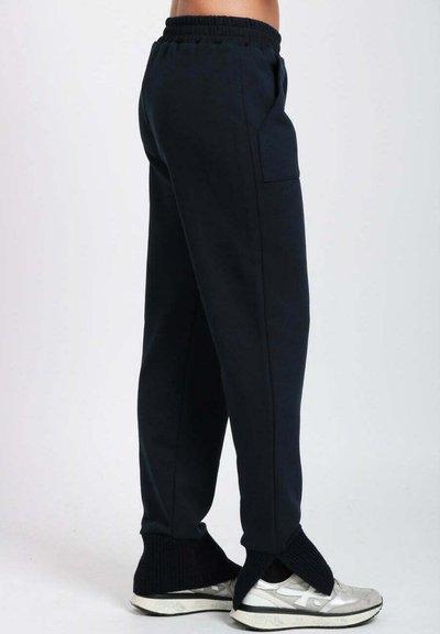 Pantaloni sportivi blu navy con vita elastica, tasche laterali e polsini alla caviglia a coste. Indossati con sneaker argento con dettagli neri.