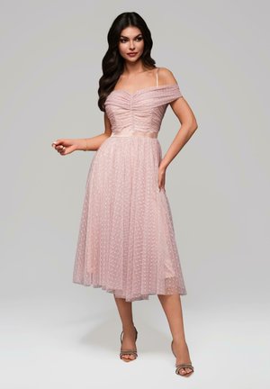 Vestido rosa off-the-shoulder con corsé fruncido, superposición de lunares transparentes y falda acampanada, con una cinta en la cintura y tirantes ajustables.